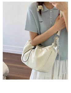 Detail of cream white drawstring shoulder bag featuring a silver metal heart pendant