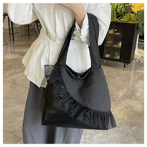 Close-up of black denim tote bag featuring decorative lace trim and leather patchwork