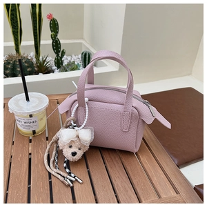Détail d'un mini sac à main en cuir grainé rose avec un charm ours en peluche sur bois