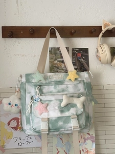 Green tie-dye canvas backpack with plush charms hanging on a white textured wall
