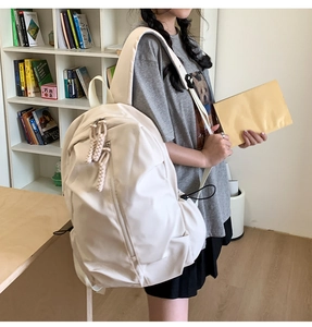 Detail of a large cream-colored casual backpack with woven rope zipper on a bookshelf background