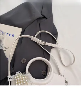 Detail of white crocodile texture handbag with pearl lace charm on grey blazer background