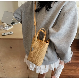 Détail du petit sac bandoulière jaune tressé avec pendentif métallique en forme de grain