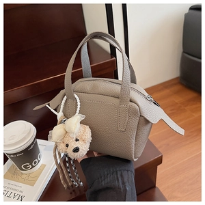 Détail d'un sac à main en cuir grainé gris avec breloque ours sur un escalier en bois
