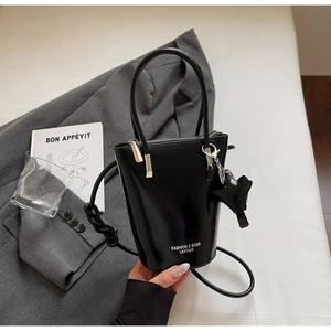 Detail of black glossy leather bucket bag with silver hardware and cat charm pendant