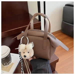 Détail du sac à main en cuir marron foncé avec pendentif ours en peluche sur bois