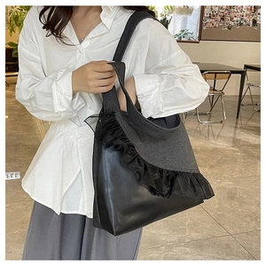 Detail view of large black denim tote bag with elegant mesh ruffles and leather trim