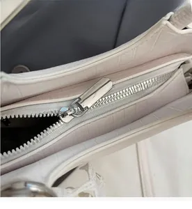 Detail of silver metal zipper and white crocodile embossed texture on a bucket bag