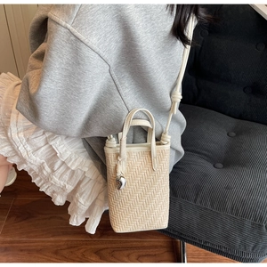Détail du sac seau tissé crème montrant la texture en V et le charme en métal en forme de cœur