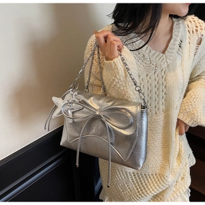 Détail d'un sac bandoulière argenté avec nœud et breloque étoile porté par un mannequin