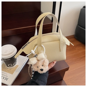 Détail d'un mini sac à main jaune crème en cuir avec un charme d'ours en peluche