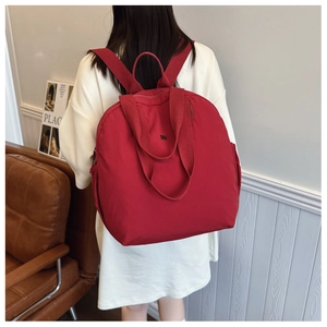 Detail of dark red waterproof nylon backpack shown on a model in a minimal indoor setting
