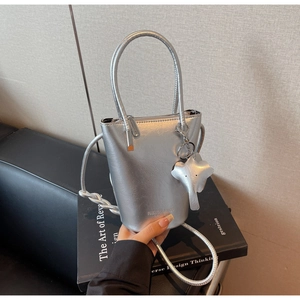Detail of silver metallic bucket bag featuring leather elephant charm and long handles