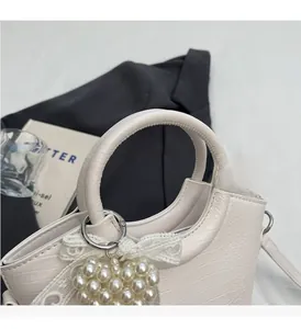Detail of white crocodile embossed handbag with pearl heart charm and lace bow decoration