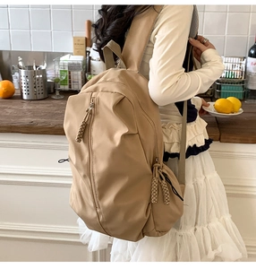 Detail of khaki nylon backpack with woven zipper pulls and multiple compartments