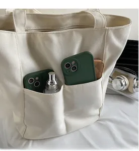 Detail of canvas tote bag showing two front utility pockets with items for storage