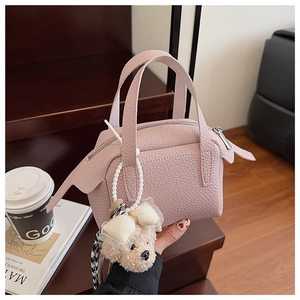 Vue détaillée d'un sac à main rose clair à texture de litchi avec breloque d'ours en peluche