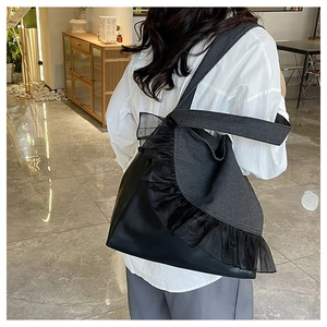 Detail view of black denim tote bag featuring layered mesh ruffles and wide shoulder strap
