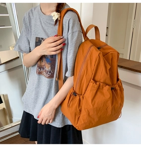 Detail of vibrant orange nylon backpack featuring drawstring side pockets and wrinkled texture