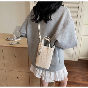 Détail d'un sac seau tressé avec breloque boule dorée et bandoulière élégante