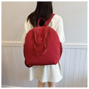 Rear view of large red nylon travel backpack worn by a model in a minimal white setting