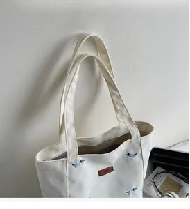 Close-up of white canvas tote bag with blue dachshund embroidery and brown leather logo tag