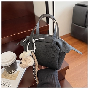 Gros plan du sac à main en cuir grainé noir avec design ailé et breloque ourson
