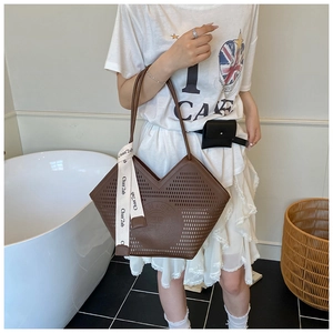 Detail of a brown hollowed leather tote bag with a decorative beige silk scarf handle