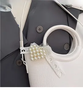 Close-up of white croc-embossed handbag with round handle and pearl heart charm decor