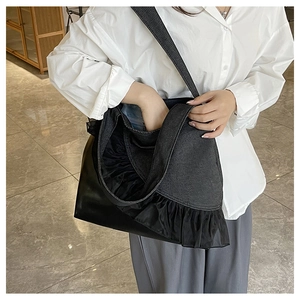 Detail view of denim tote bag with black lace trim and faux leather bottom panel