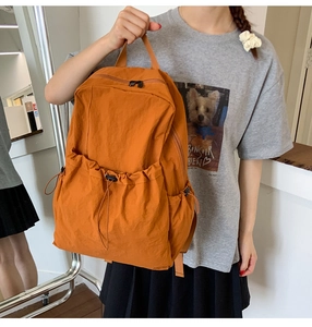 Detail of caramel nylon backpack featuring a drawstring front pocket and side compartments