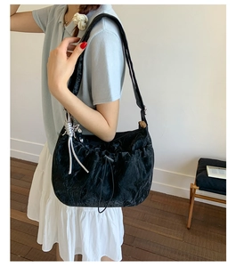 Detail of black pleated shoulder bag featuring a silver butterfly pendant and drawstring closure
