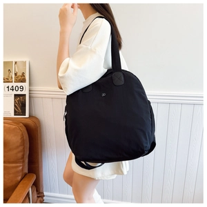 Detail view of large black waterproof nylon tote bag with metal logo on model's shoulder
