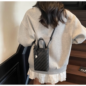 Détail du sac seau tressé noir avec breloque argentée et bandoulière à nœud décoratif