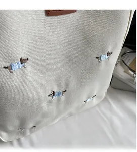Close-up of creamy white canvas bag featuring cute embroidered puppies and leather patch