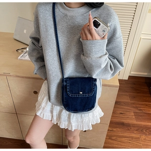 Detail of dark blue denim crossbody bag with metal snap button closure and slim strap