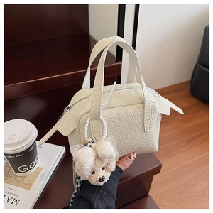 Détail d'un mini sac à main beige grainé avec un pendentif ours en peluche sur la fermeture