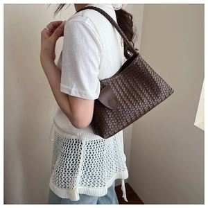 Detail of hand-woven dark brown leather shoulder bag with intricate texture and round seal