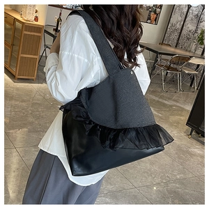 Detail of large denim and leather tote bag with mesh ruffles on an indoor model
