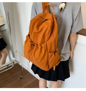 Detailed view of an orange nylon backpack featuring a drawstring front pocket and smooth zippers