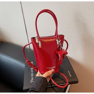 Close-up of glossy red patent leather bucket bag with elephant charm and strap