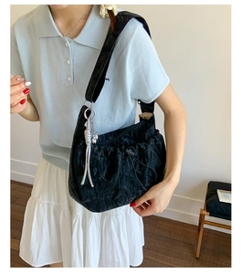 Detail of black pleated shoulder bag with silver metallic woven rope pendant detail