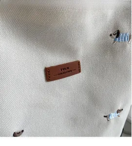 Detail of embroidered puppy on white canvas tote bag with a brown leather logo patch