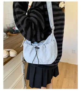 Detail of light blue pleated dumpling bag with drawstring and wide strap on a model
