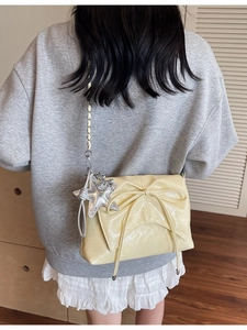 Sac bandoulière en cuir verni jaune avec nœud et breloque étoile porté par un modèle