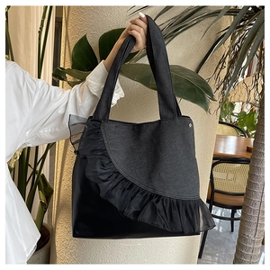 Detail of a black denim tote bag with sheer mesh ruffles and a spacious interior design