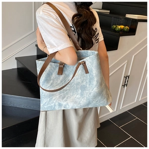 Detail of light blue washed denim tote bag with brown leather straps for commuting