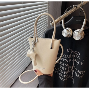 Detail view of cream bucket bag with metal logo and stylish strap for women