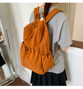 Side view of orange nylon backpack showing adjustable drawstring side pocket and texture
