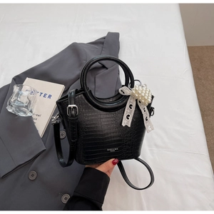 Detail of black crocodile texture handbag with pearl pendant and lace bow decoration